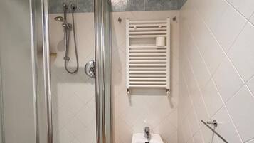 Un bagno con doccia vetrata, un lavandino a colonna bianco e un portascopevoli.