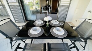 Uma sala de jantar com mesa e cadeiras pretas, um vaso com flores e vista para o exterior.