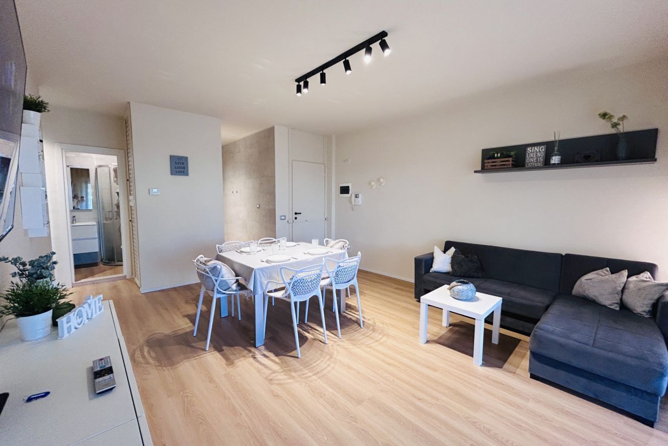 Un salon moderne comprenant un coin repas, un canapé noir et une petite table sur laquelle est posé un vase.