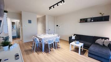 Un salon moderne comprenant un coin repas, un canapé noir et une petite table sur laquelle est posé un vase.