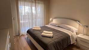 Quarto com cama grande, mesa de cabeceira com abajur e cortinas finas.