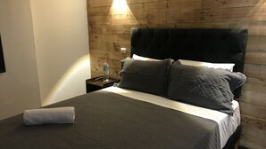 A bed with a dark quilted bedspread, two pillows, and a folded towel on a wooden headboard. - Santa Maria Express (Santiago)