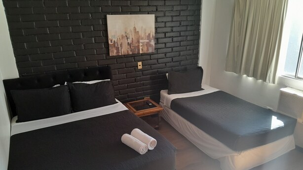 A hotel room with two beds, a black brick wall, and a cityscape painting. - Santa Maria Express (Santiago)