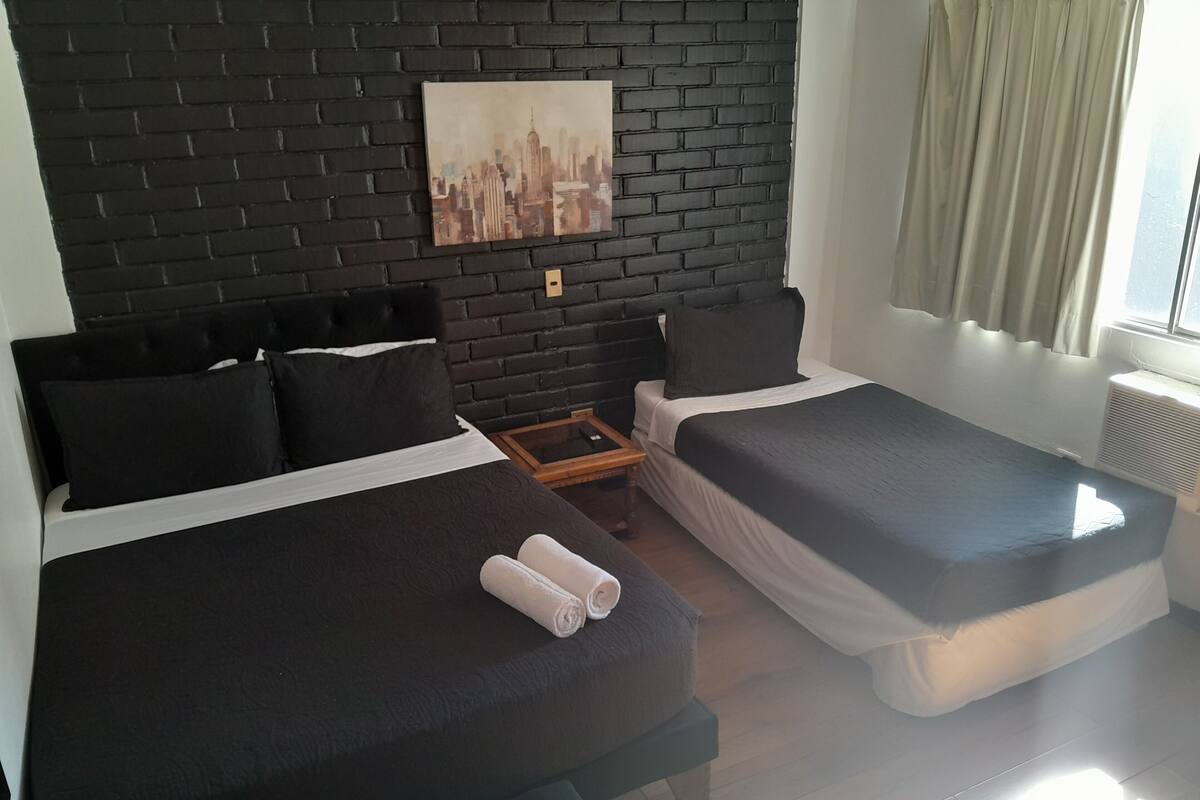 Une chambre d’hôtel avec deux lits, un mur en briques noires et un tableau représentant un paysage urbain.