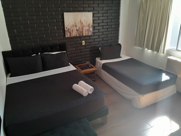 A hotel room with two beds, a black brick wall, and a cityscape painting.