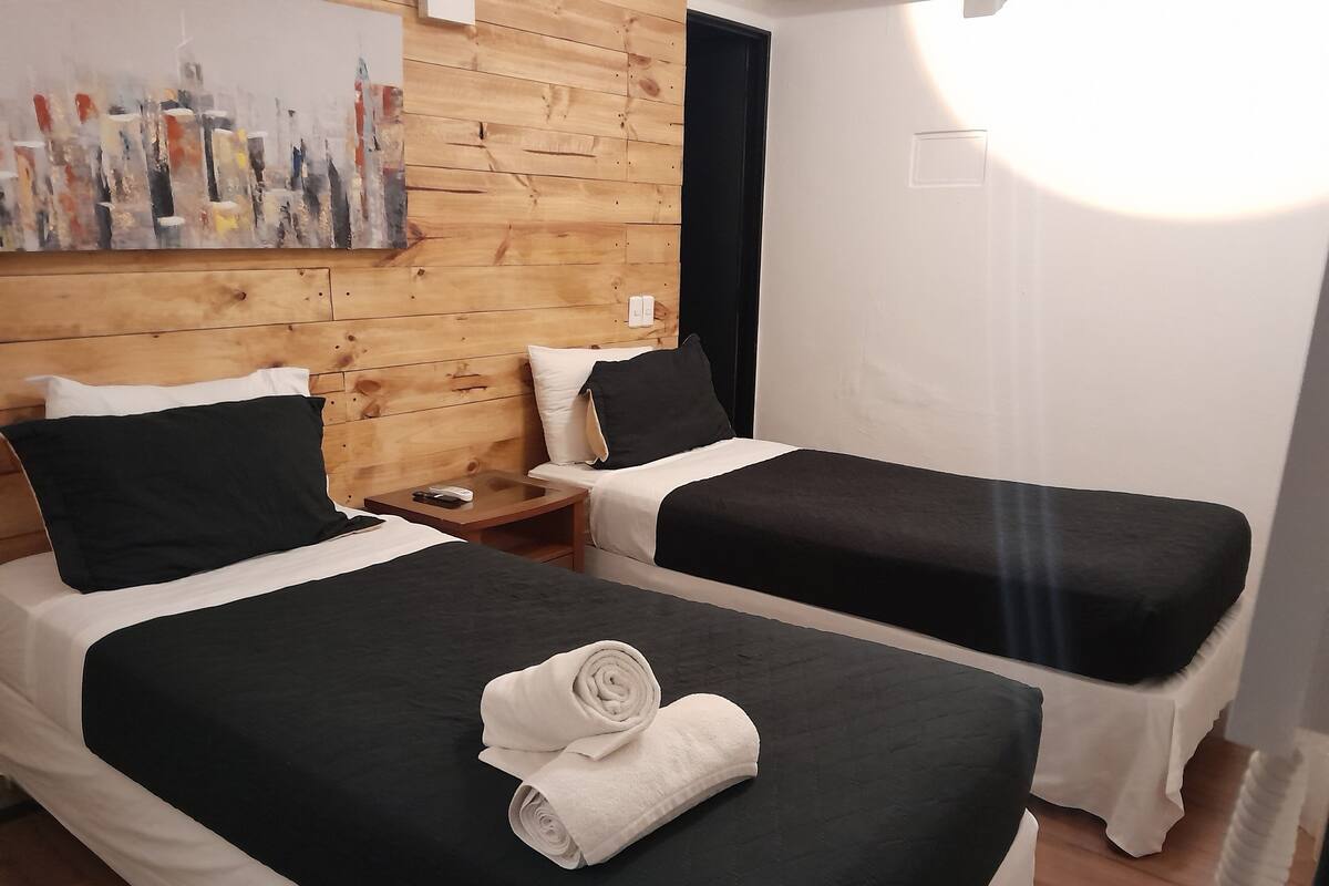 Une chambre d’hôtel avec deux lits, des lambris en bois aux murs, un tableau et une table de chevet avec un téléphone et une télécommande.
