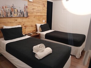 A hotel room with two beds, wooden paneling on the walls, a painting, and a nightstand with a phone and remote control.