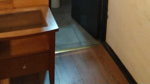 A wooden wall with a white switch, a wooden bench, and a black door leading to a bathroom with a sink and mirror. - Santa Maria Express (Santiago)