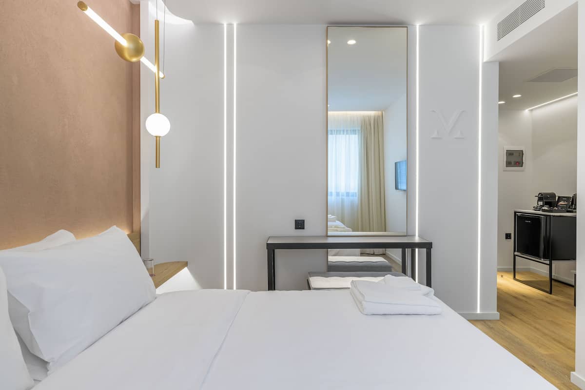 A modern hotel room with a large bed, a bedside table, a mirror, and a desk with a chair.