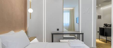 Une chambre d’hôtel moderne avec un grand lit, une table de chevet, un miroir et un bureau avec une chaise.