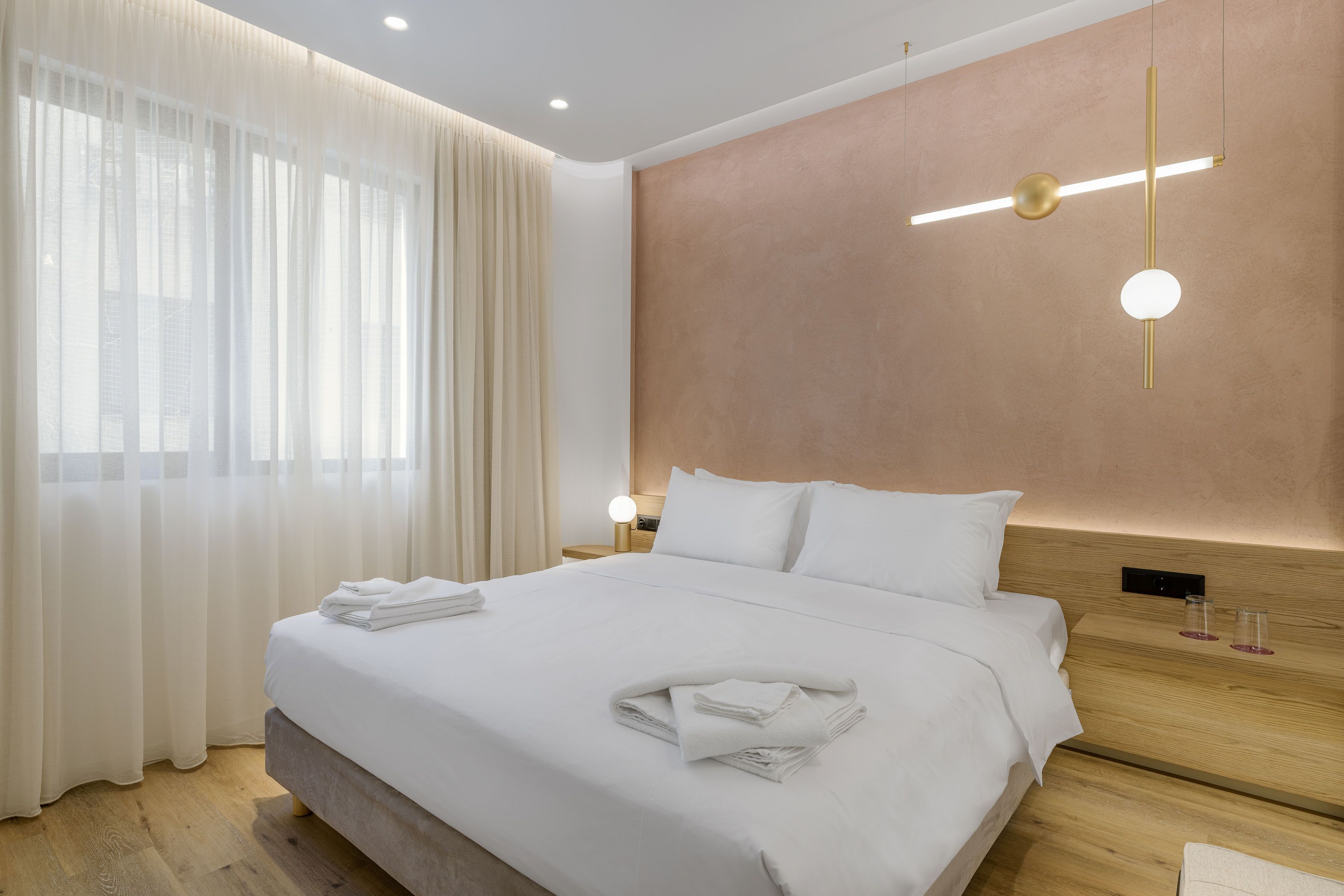 A modern hotel room with a neatly made bed, a wooden headboard, and a wall-mounted light fixture.