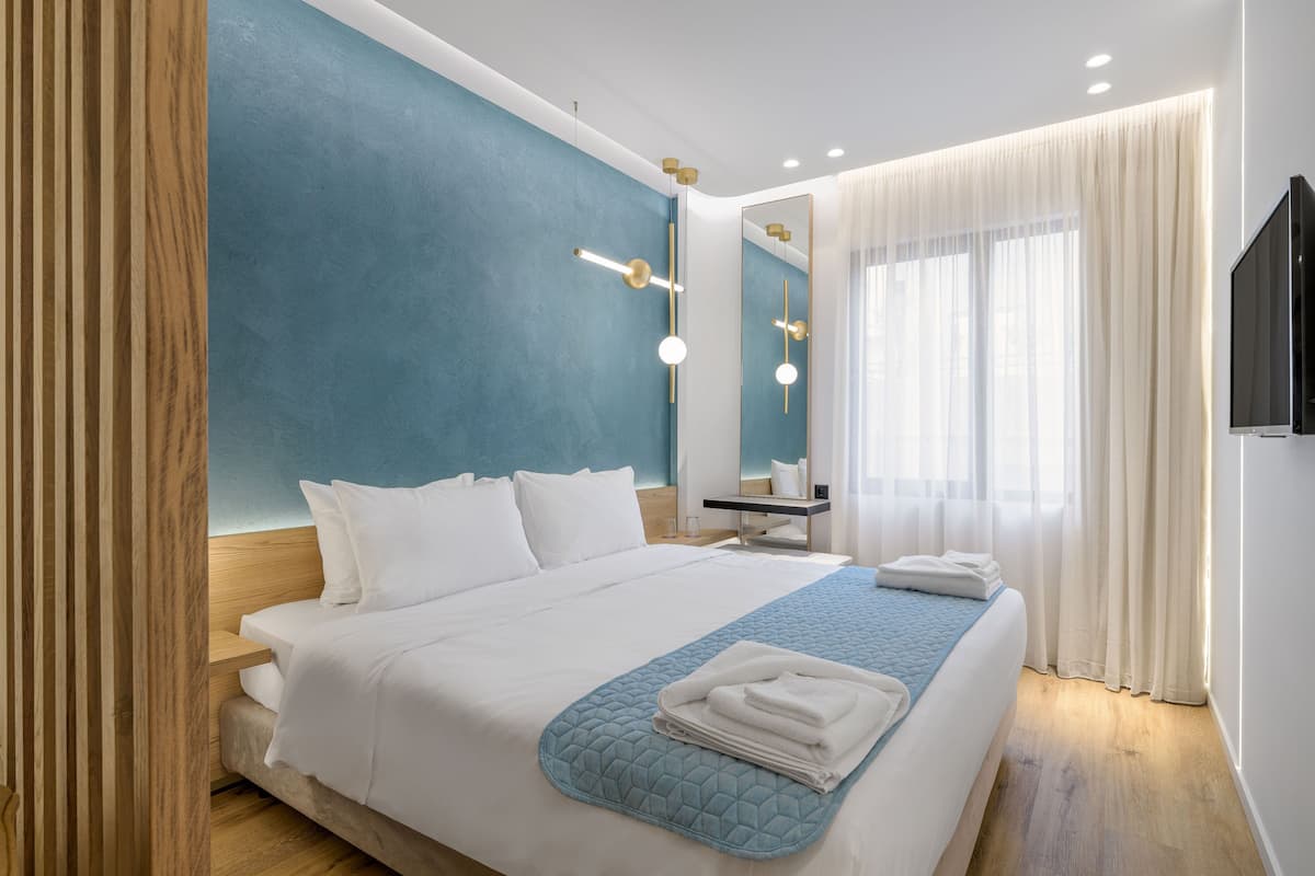 A modern hotel room with a large bed, a wooden nightstand, a bathroom mirror, and a TV mounted on the wall.