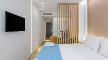 A modern hotel room with a large bed, a flat-screen TV mounted on the wall, a wooden partition, and a small table with a chair.