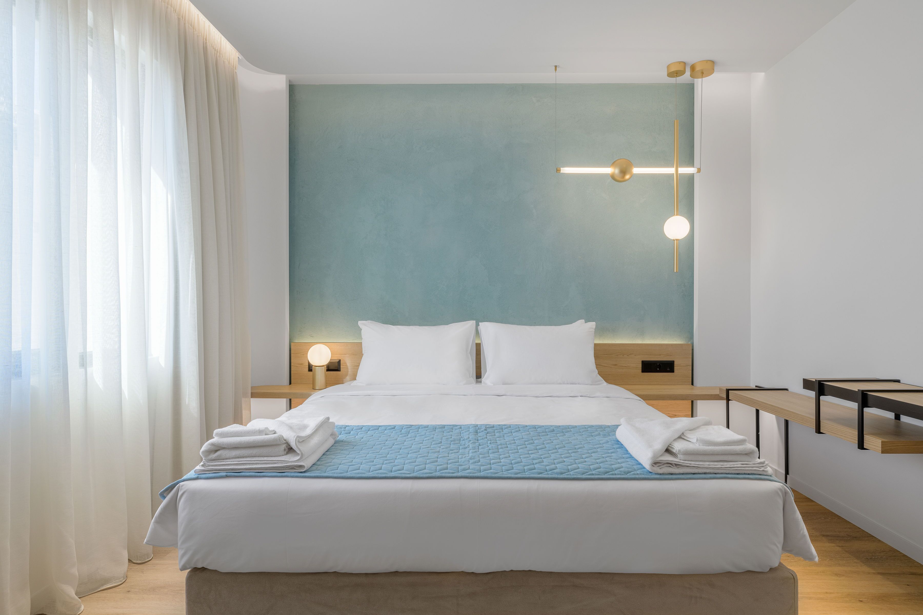 A modern hotel room with a large bed, white linens, a blue quilt, and a bedside table with a lamp.