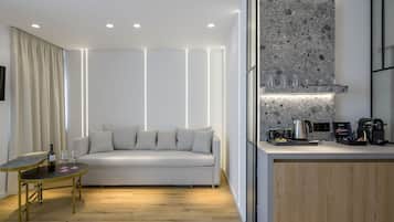 Una sala de estar moderna con un sofá, una mesita con copas de vino y una cocina con encimera y electrodomésticos.
