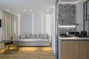 A modern living room with a sofa, a small table with wine glasses, and a kitchen area with a countertop and appliances.