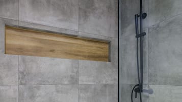 Um chuveiro moderno com porta de vidro, azulejos cinzas e prateleira de madeira.