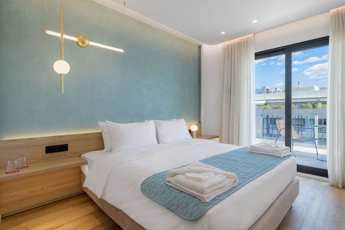A modern hotel room with a large bed, a view of the city, and a balcony with outdoor seating.