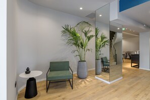 A modern office space with a green chair, a round table, and two large potted plants.