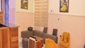 A living room with a sofa, armchairs, a coffee table, and a TV stand. - Fisher Suites and Apartment (Abuja)