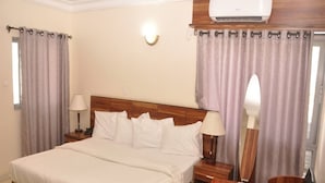 A hotel room with a large bed, two bedside tables with lamps, a small wooden side table, and a chair. - Fisher Suites and Apartment (Abuja)