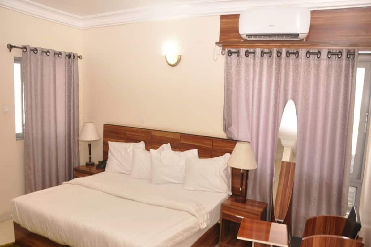 A hotel room with a large bed, two bedside tables with lamps, a small wooden side table, and a chair.