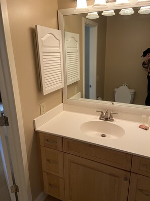 A bathroom with a white sink, wooden cabinets, a mirror, and a toilet.