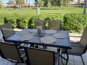 Ett bord uppdukat utomhus med fyra stolar, ett glas iste och servetter.