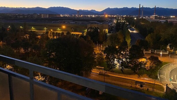 A cityscape at dusk with illuminated buildings, a highway, and mountains in the background. - Camilla 's House 2 - “it's cool“. (Torino)