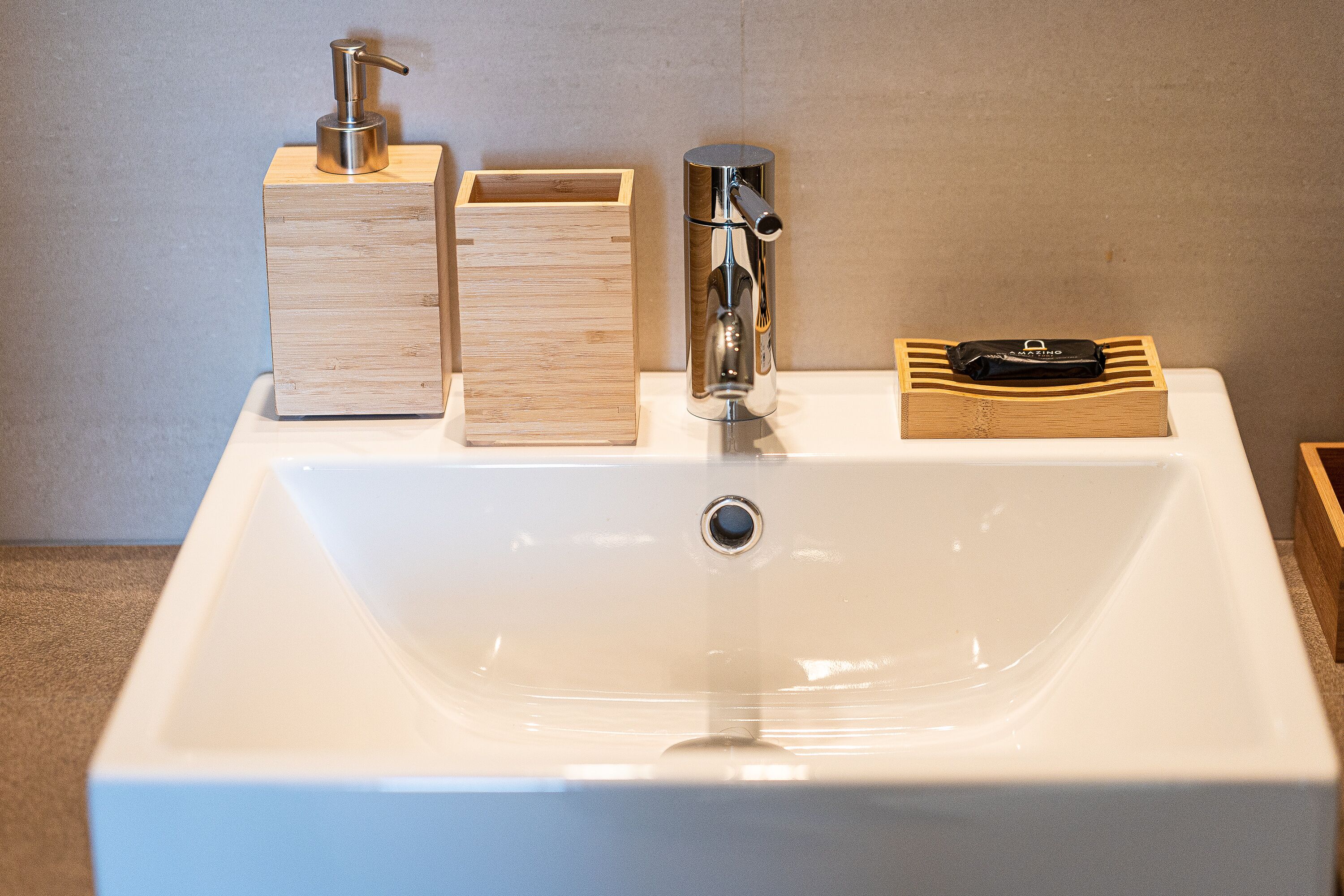 A white bathroom sink with a chrome faucet, a wooden soap dispenser, and a soap dish.