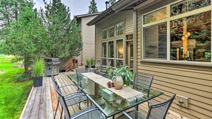 Une terrasse dotée d’une table et de chaises à plateau en verre, entourée d’une autre terrasse en bois et d’une pelouse.