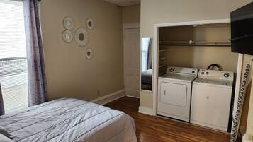 Une chambre avec un lit, un ventilateur de plafond, une fenêtre avec des rideaux et un espace buanderie équipé de deux machines à laver.