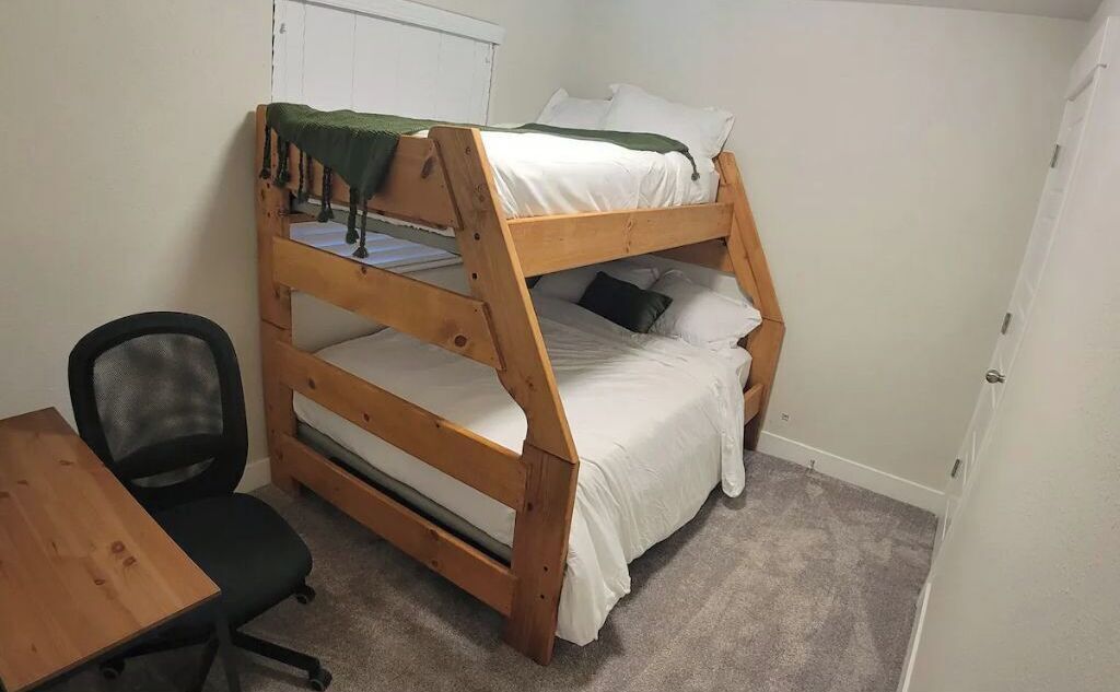 A bunk bed room with a desk and chair, carpeted floor, and white walls.