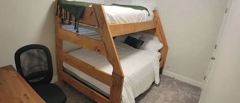 A bunk bed room with a desk and chair, carpeted floor, and white walls.