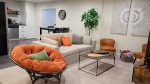 Uma sala de estar moderna com sofá, poltrona, mesa de centro e um espaço de jantar com cadeiras e mesa.