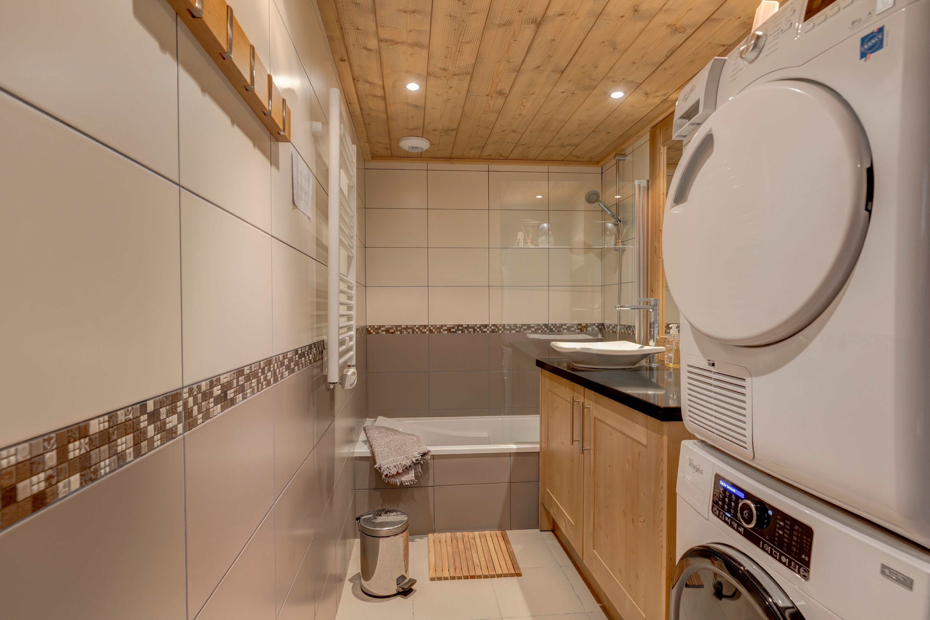 A modern bathroom with a wooden ceiling, a bathtub, a washing machine, and a sink.