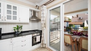 Et moderne køkken med hvide skabe, en sort bordplade og en gasblus. Der er en skydedør af glas, der fører ud til en balkon med et bord og stole.