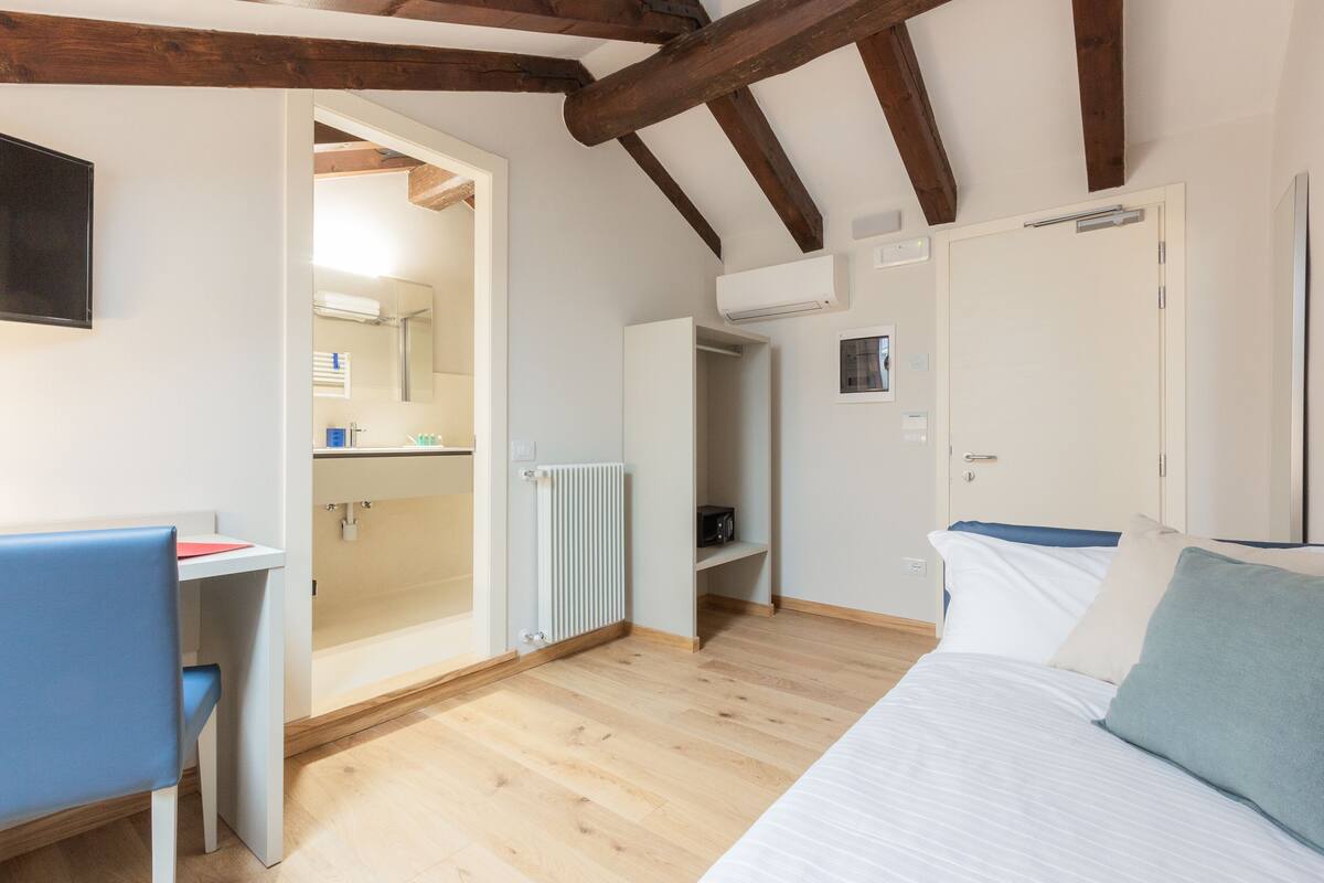 Une chambre à coucher avec un lit, un bureau et une chaise. On y trouve également une armoire et un radiateur.