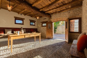 Um quarto rústico com parede de pedra, vigas de madeira no teto, uma mesa de madeira com um vaso e um banco com almofadas.