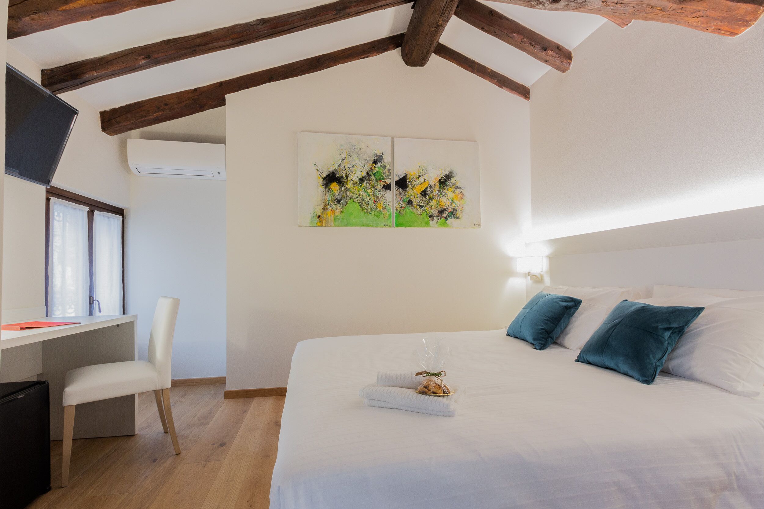 Une chambre à coucher avec un lit, deux oreillers, un bureau avec une chaise et un tableau accroché au mur.
