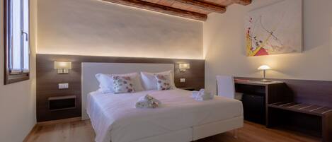 A neatly arranged bedroom with a large bed, bedside tables, a desk, and a painting on the wall.