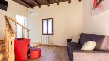 Una sala de estar con una escalera de madera, un sofá rojo, un sofá gris y una ventana con persianas.