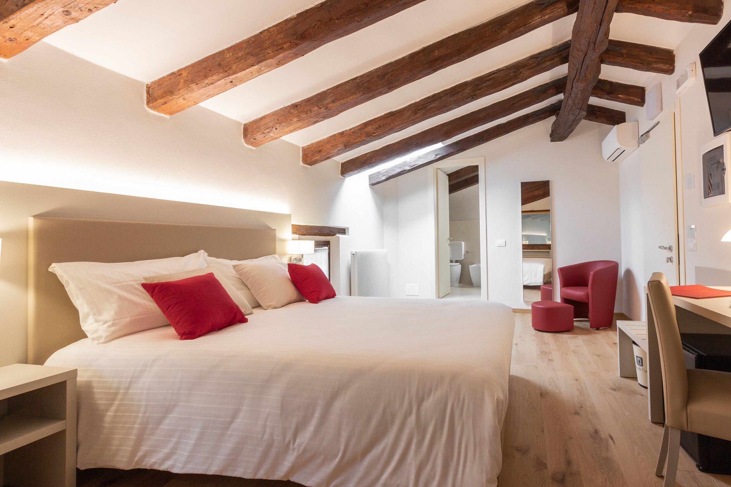 A bedroom with a large bed, wooden beams, a desk, and a chair.