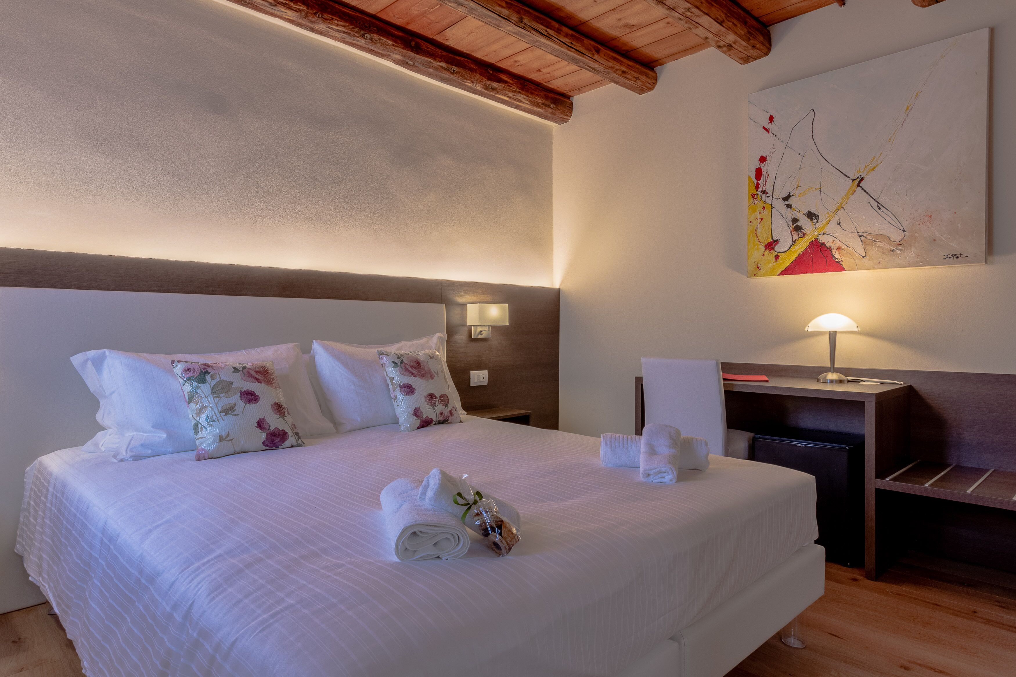 A neatly made bed with floral pillows, a bedside table with a lamp, and a painting on the wall.