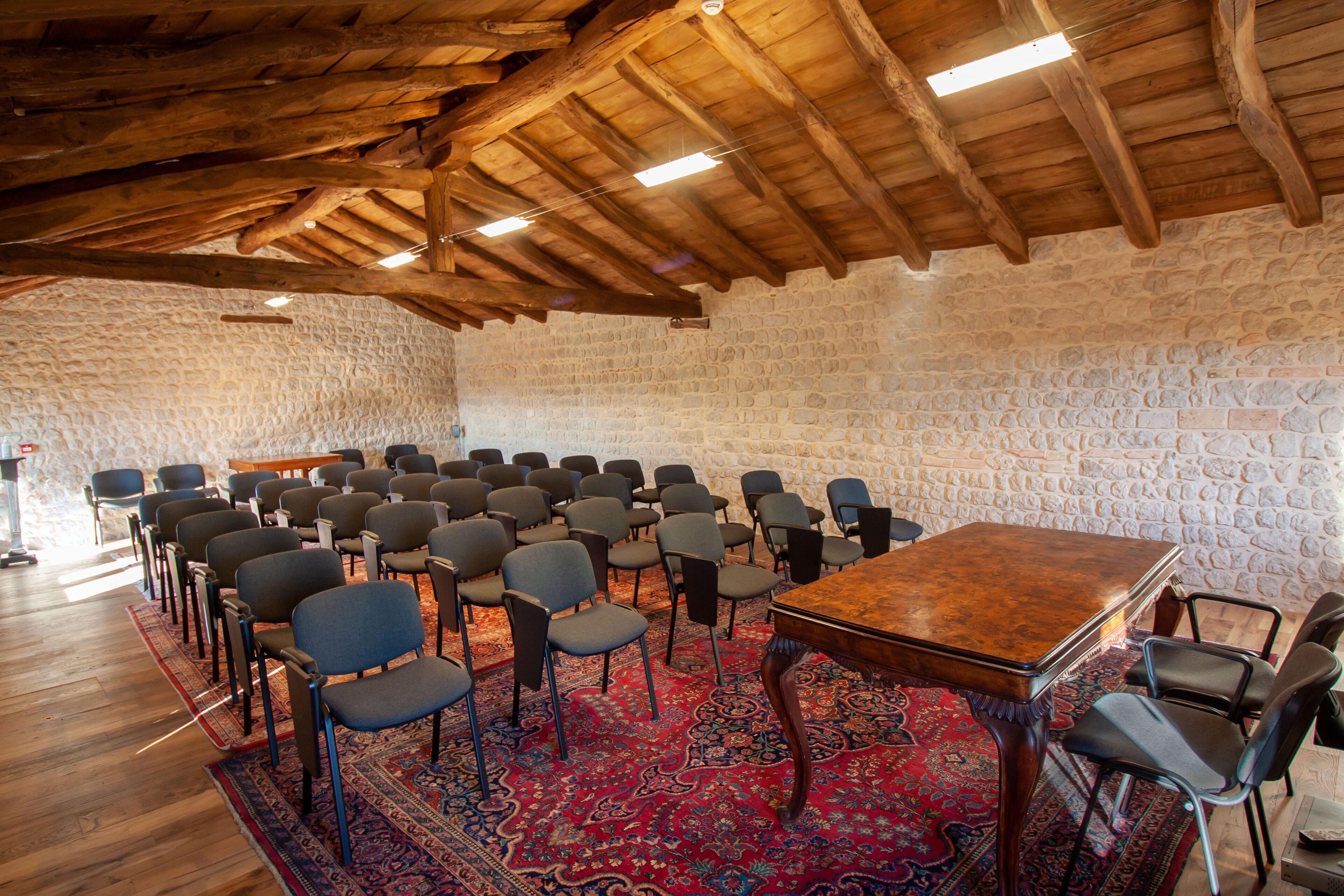 A conference room with a wooden ceiling, stone walls, and a large table surrounded by chairs.