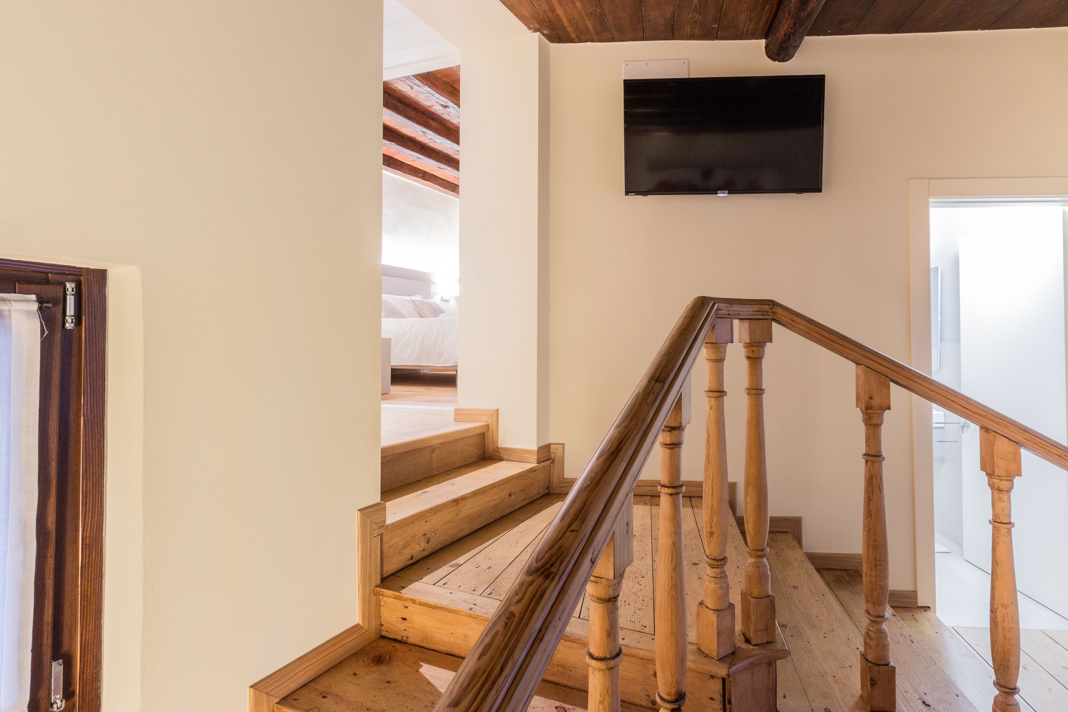 A wooden staircase with a handrail, a flat-screen TV mounted on the wall, and a door leading to another room.