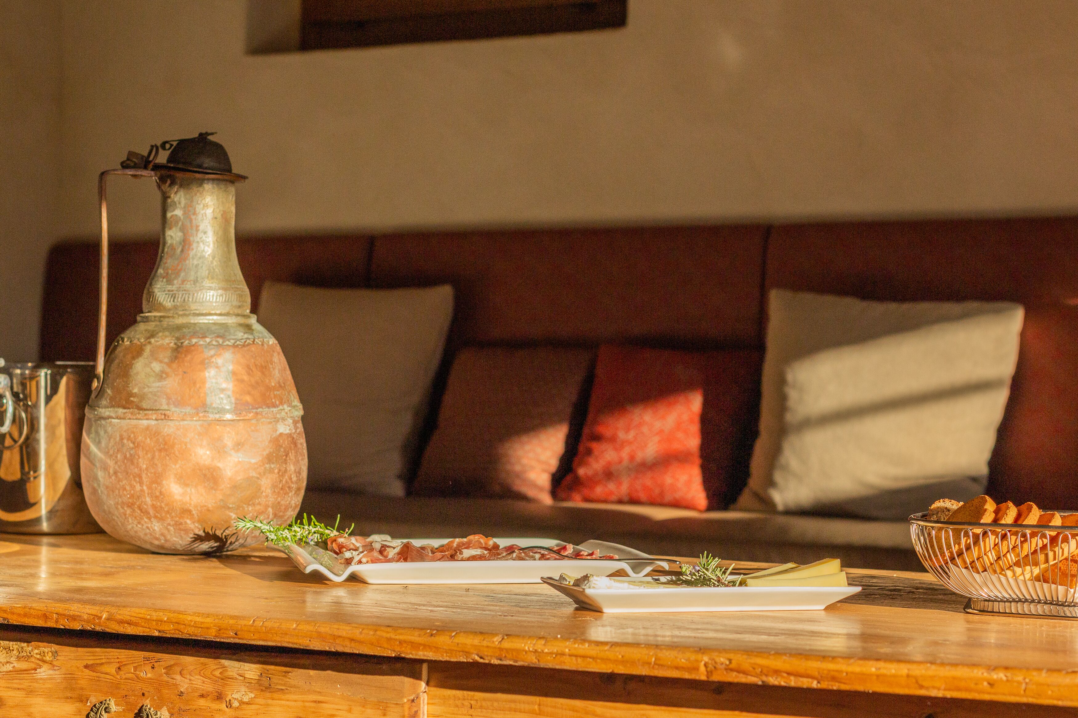 A dining table with a metal pitcher, plates of food, and a bowl of bread.