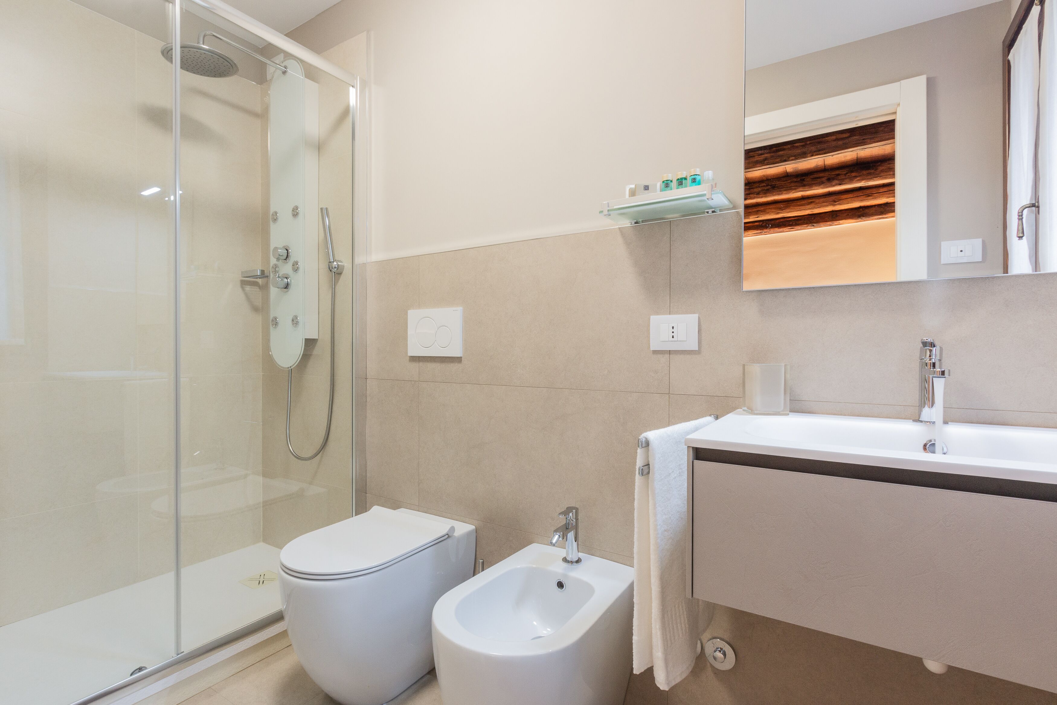 Un baño moderno con ducha de vidrio, un bidé, un lavamanos y un espejo sobre el lavamanos.
