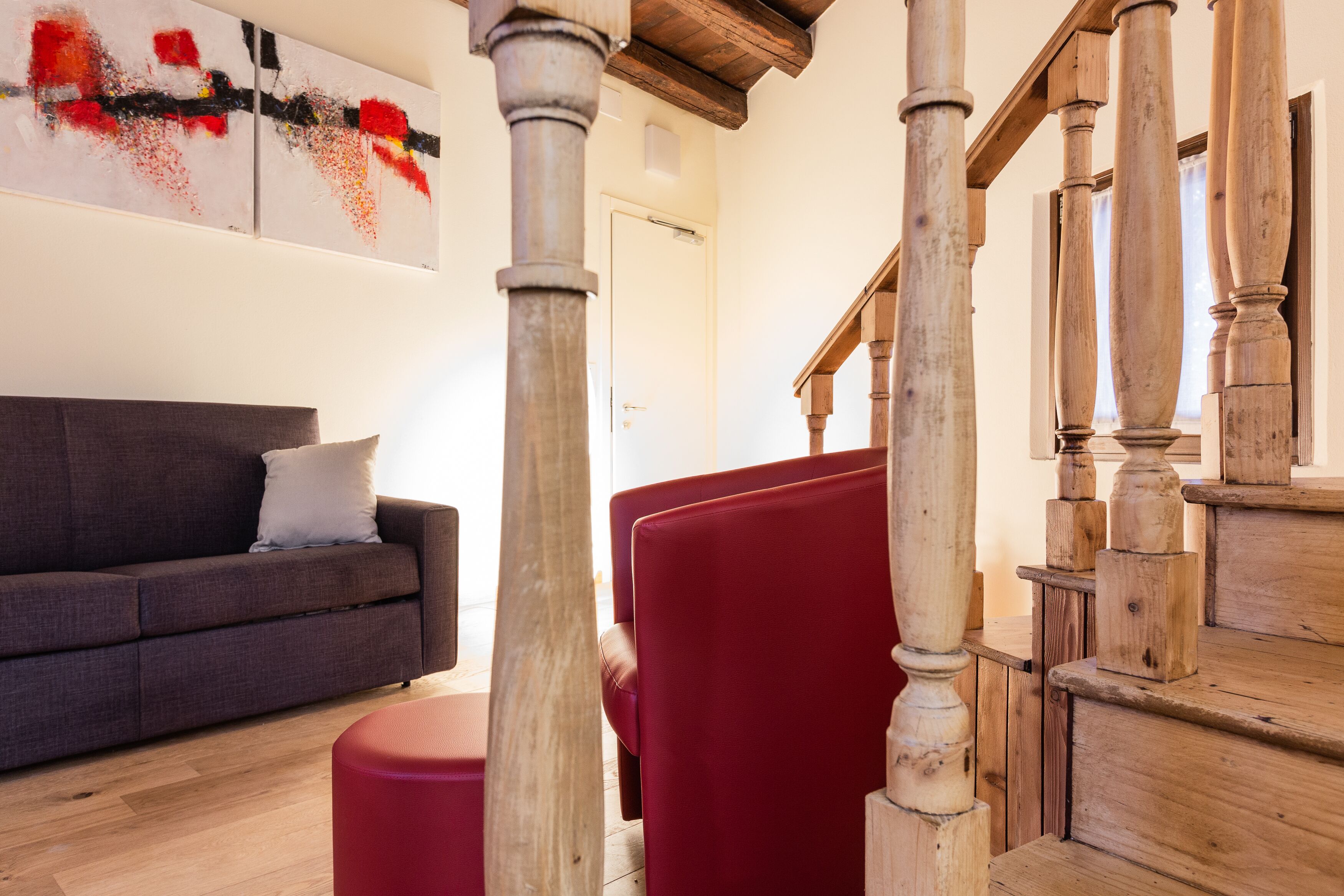 Una sala de estar con un sofá gris, una silla roja y una escalera de madera.