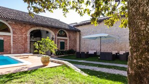 Un patio con piscina, mobiliario exterior y un edificio de piedra con arcos.